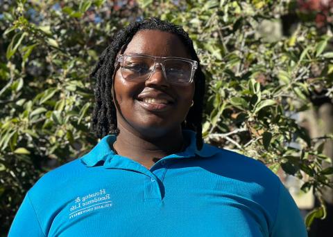 Smiling person with dreadlocks and clear glasses in a blue Tulane University Housing & Residence Life polo shirt.
