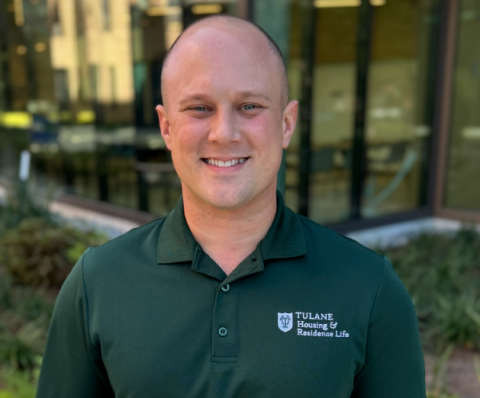 Smiling man in a dark green polo shirt with the Tulane Housing & Residential Life logo.