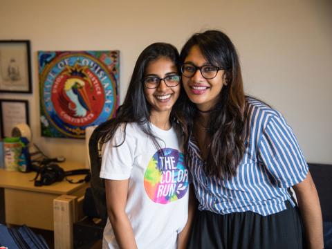 Two female students hug and pose for camera in dorm room