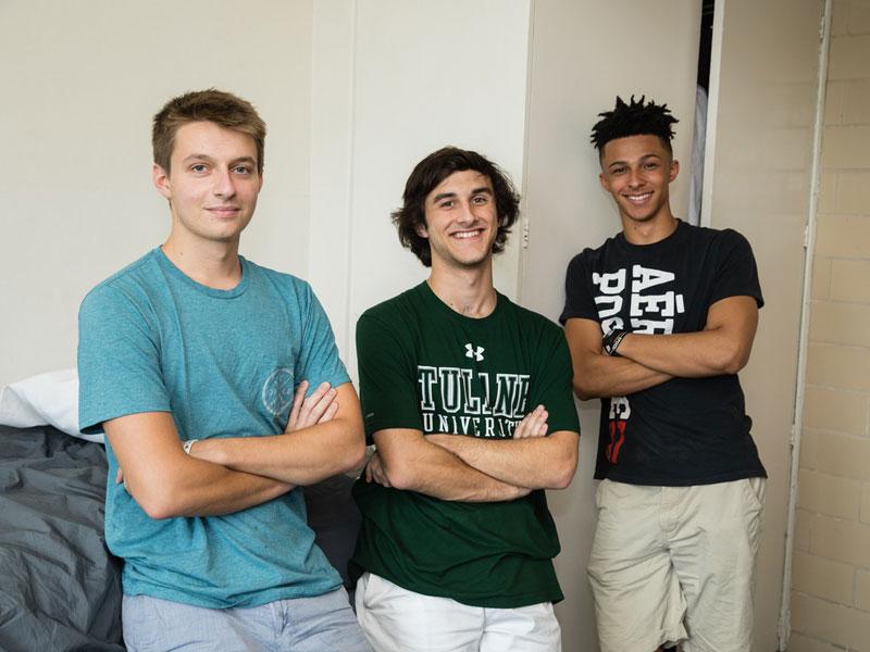 Three male students pose for photo in dorm room