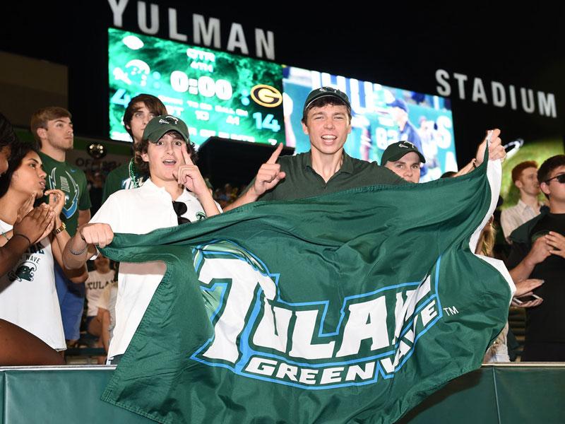 Students cheer and wave Tulane flag during football game at Yulman Stadium